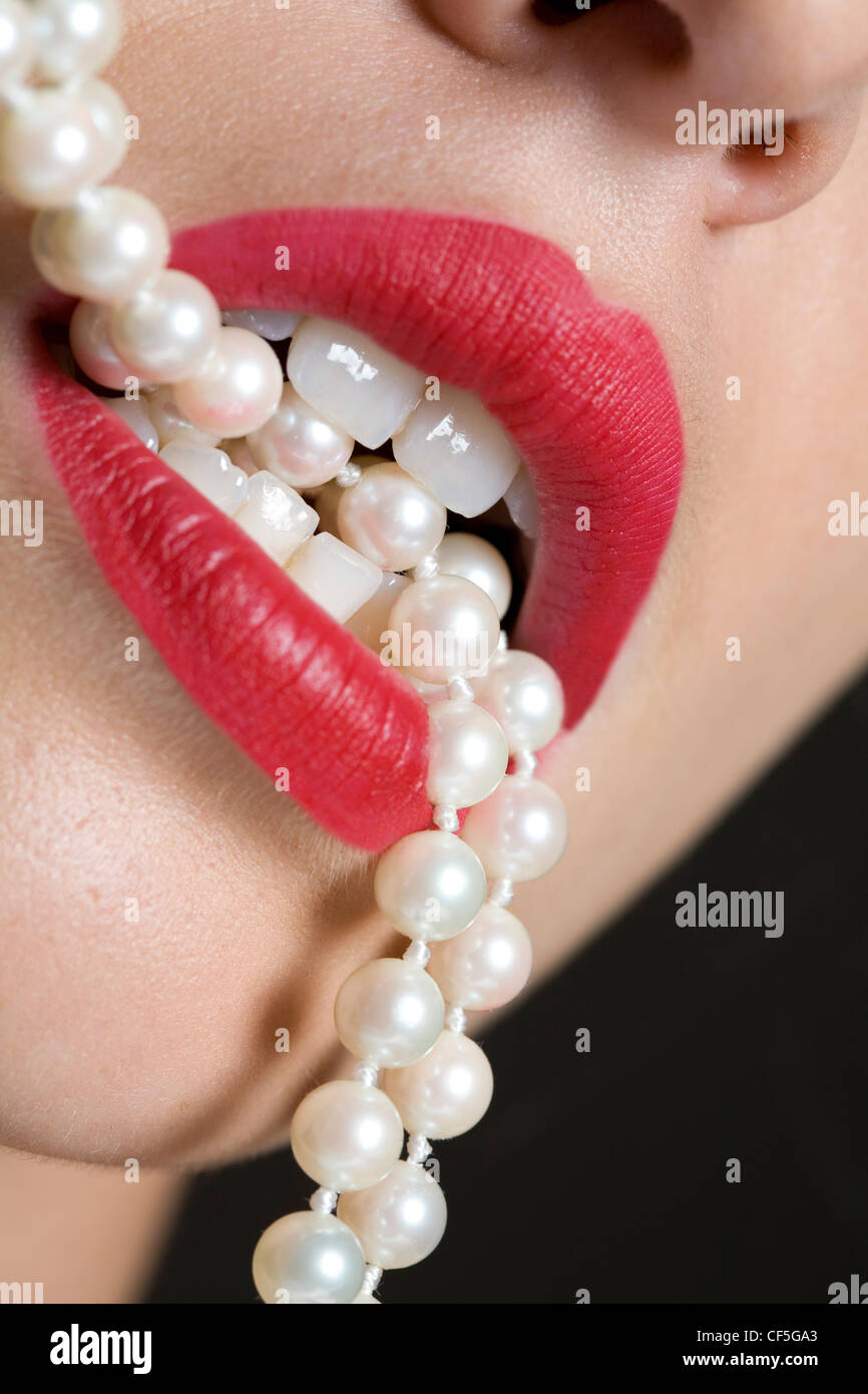 Weibchen mit tief rosa Lippenstift, beißen eine Zeichenkette der Perlen Stockfoto