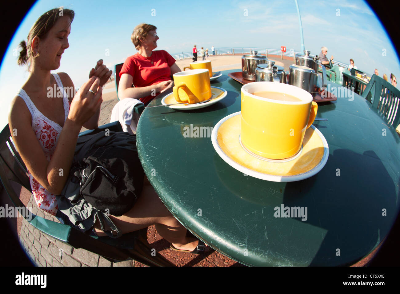 Frauen saßen an einem Tisch trinken Tassen Tee am Nachmittag auf Morecambe Meer. Stockfoto