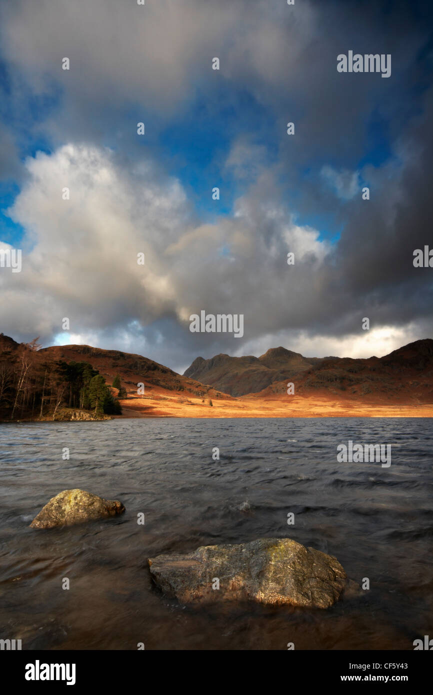 Sonnenlicht, Beleuchtung, ferne Ufer Blea Tarn, mit Blick auf die Langdale Pikes im Lake District. Stockfoto