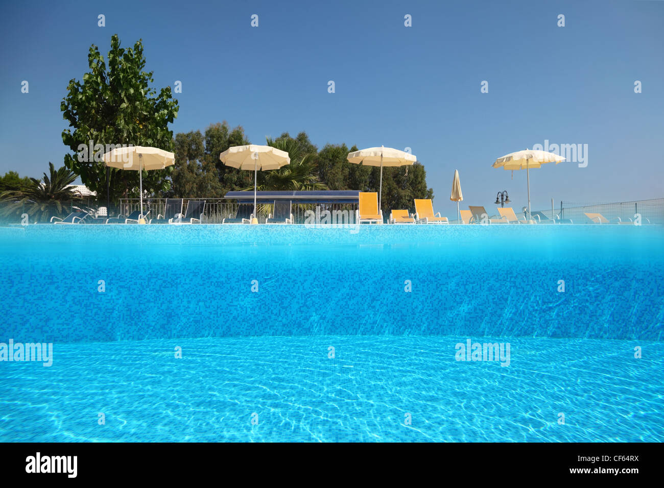 Pool unter offenen Himmel am Rand davon Liegestühle mit Sonnenschirmen, halbe Unterwasserfotografie stehen Stockfoto