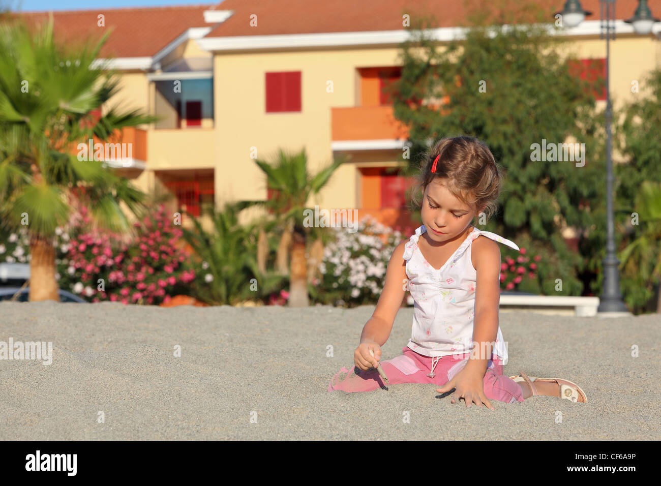 Mädchen sitzt tagsüber am Strand und dazulernen führt Stöckchen auf sand Stockfoto