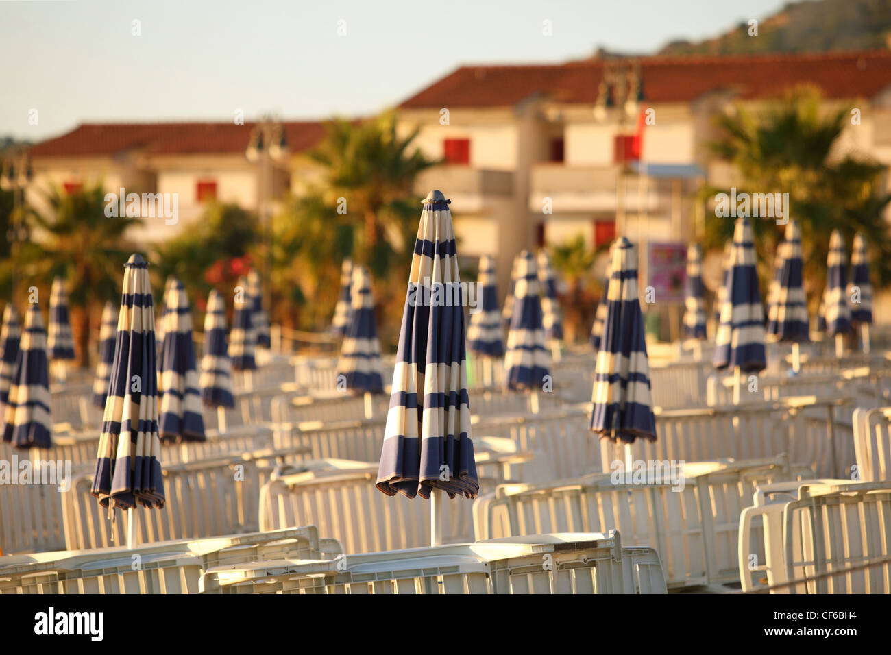 Liegestühle und Strand Sonnenschirme ordentlich gebaut Reihen am Strand morgens neben Hütten, flacher Schärfentiefe Stockfoto