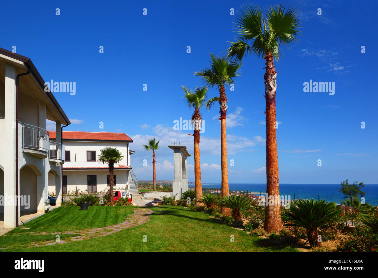 Weißes zweistöckiges Haus mit braunem Dach, grünen Rasen, Palmen an der Küste Stockfoto