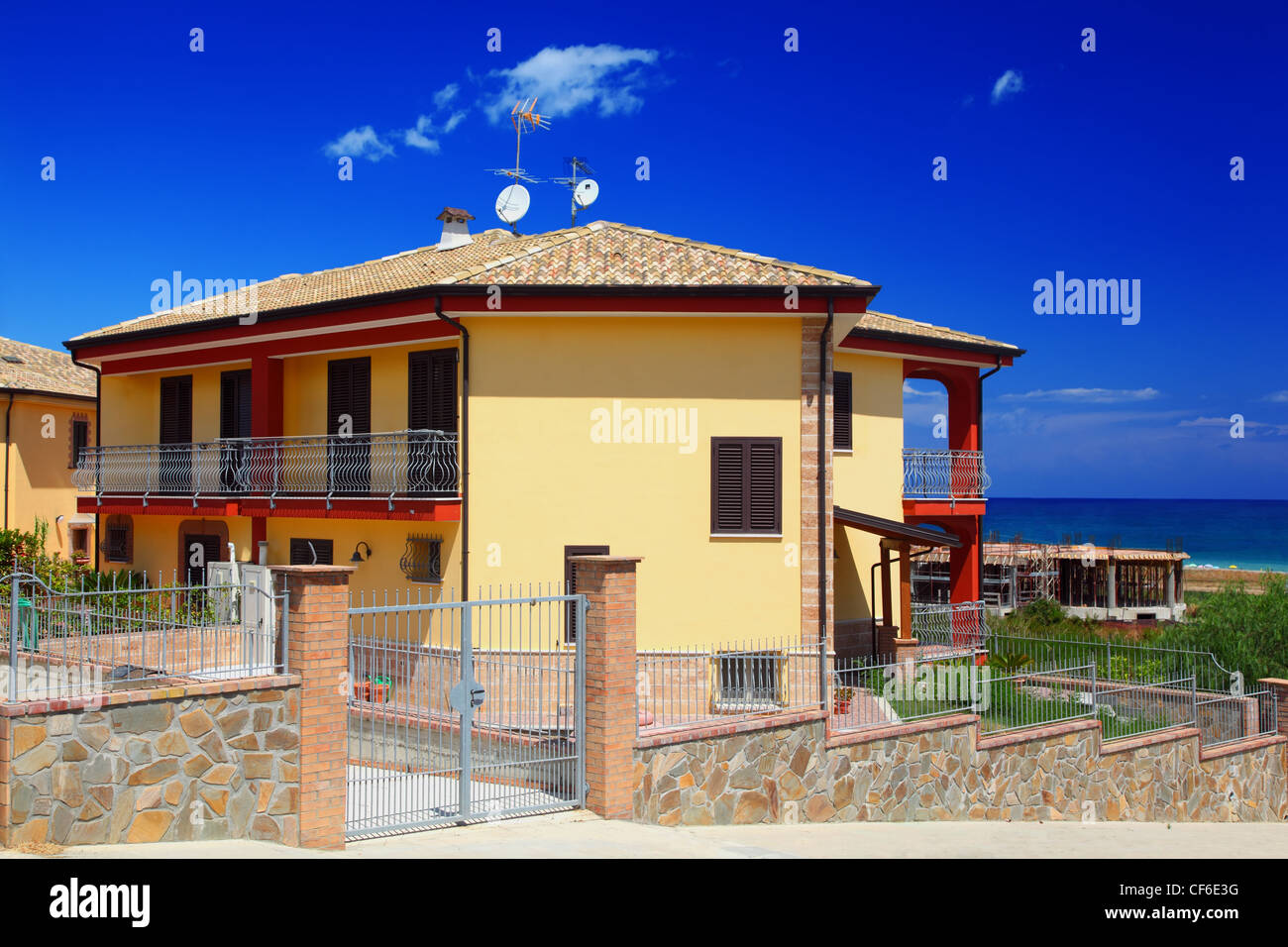 Eingezäunten gelbe zweistöckiges Ferienhaus mit Garten und Balkon an Küste Stockfoto