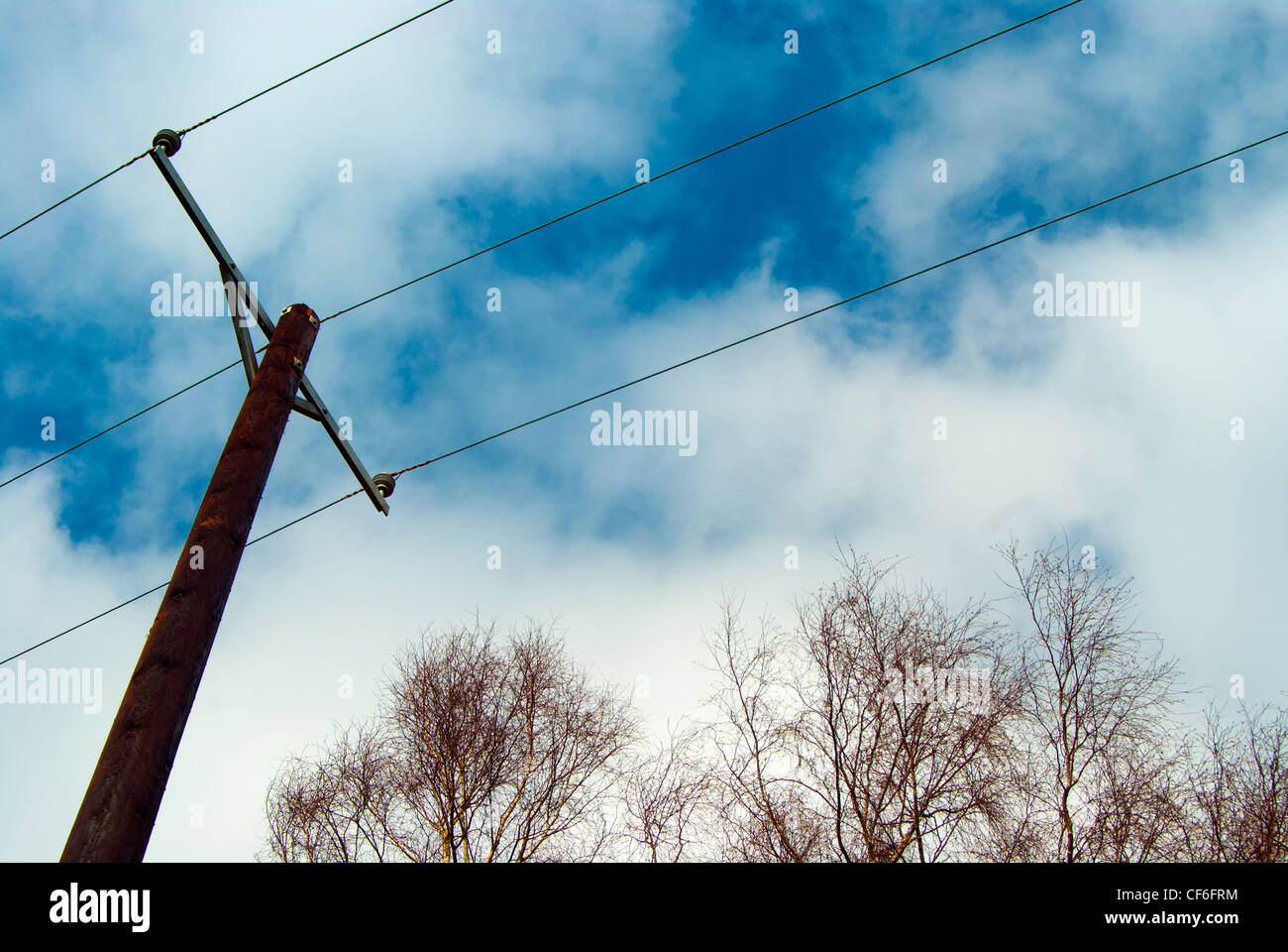Elektrizität Mast vor einem blauen & weißen Himmel mit Bäumen Stockfoto