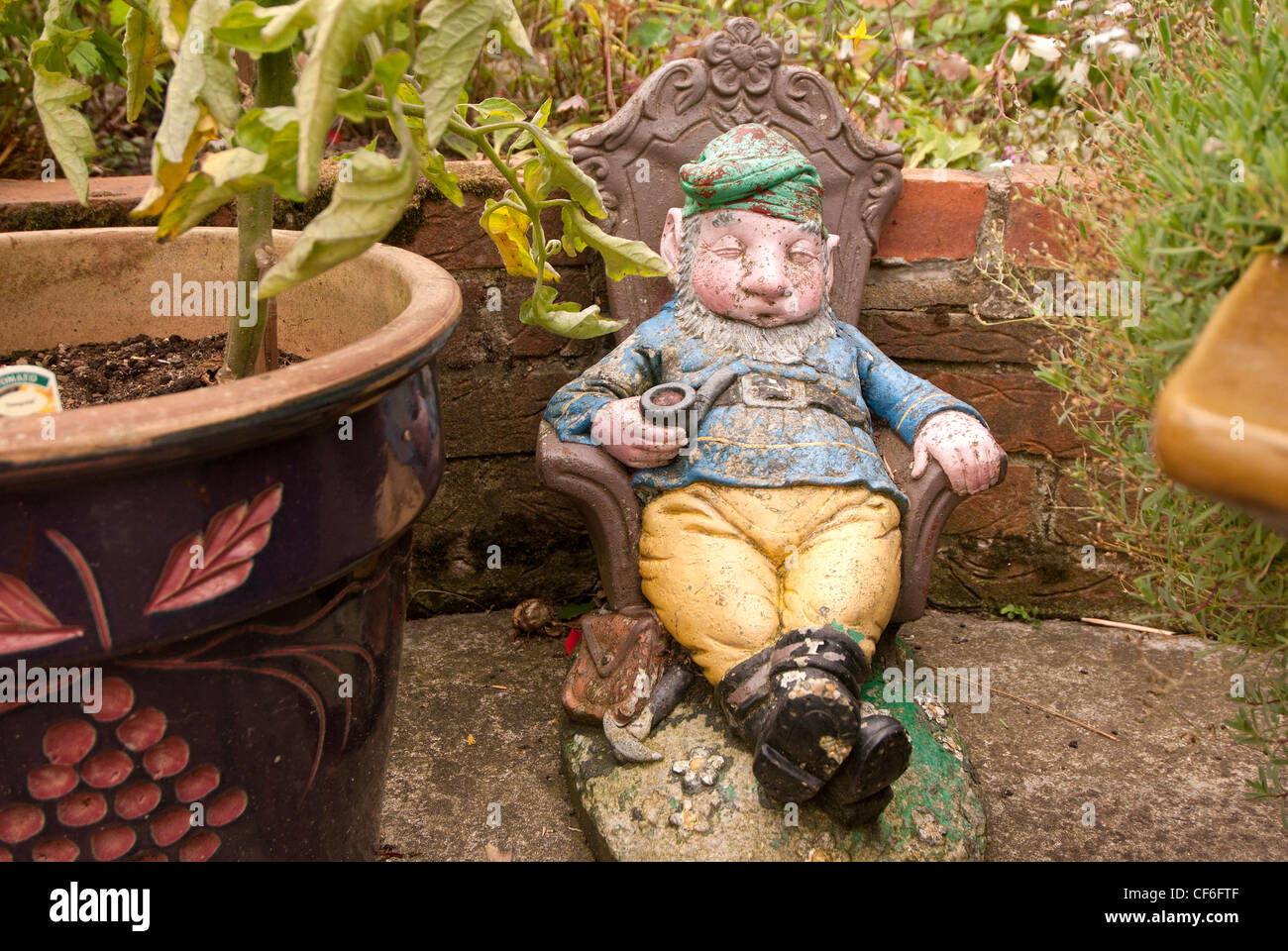 Einen dösenden Gartenzwerg, neben einem Garten Topf und im Schatten der eine Tomatenpflanze. Stockfoto