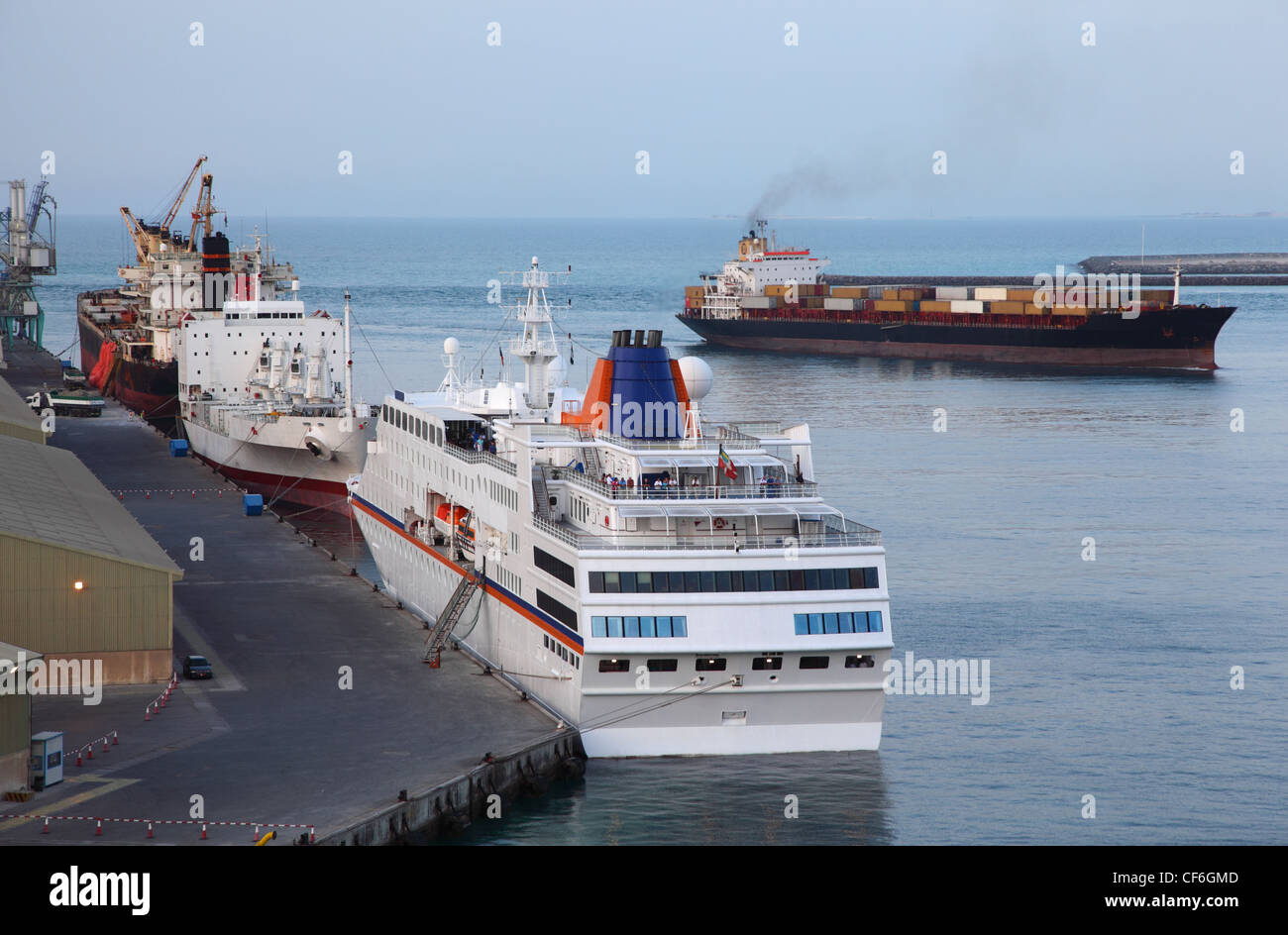 Industrielle Frachtschiffe und große weiße Kreuzfahrtschiff in einem Hafen in Abu Dhabi Stockfoto