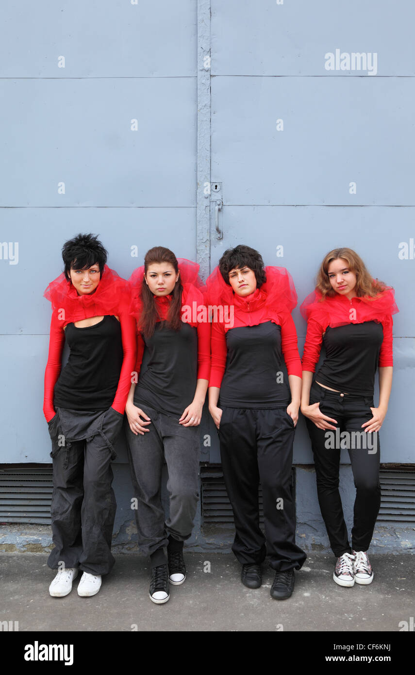 Vier Mädchen im gleichen rot-schwarze Kleider stehen und stützte sich auf blauen Wand Stockfoto