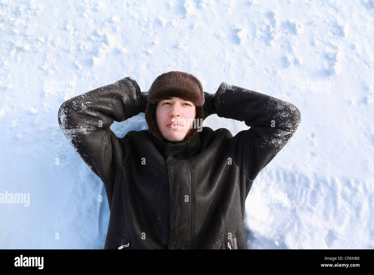 Junger Mann liegt am Rücken auf Schnee suchen Hände zum Kopf und schaut verträumt Stockfoto