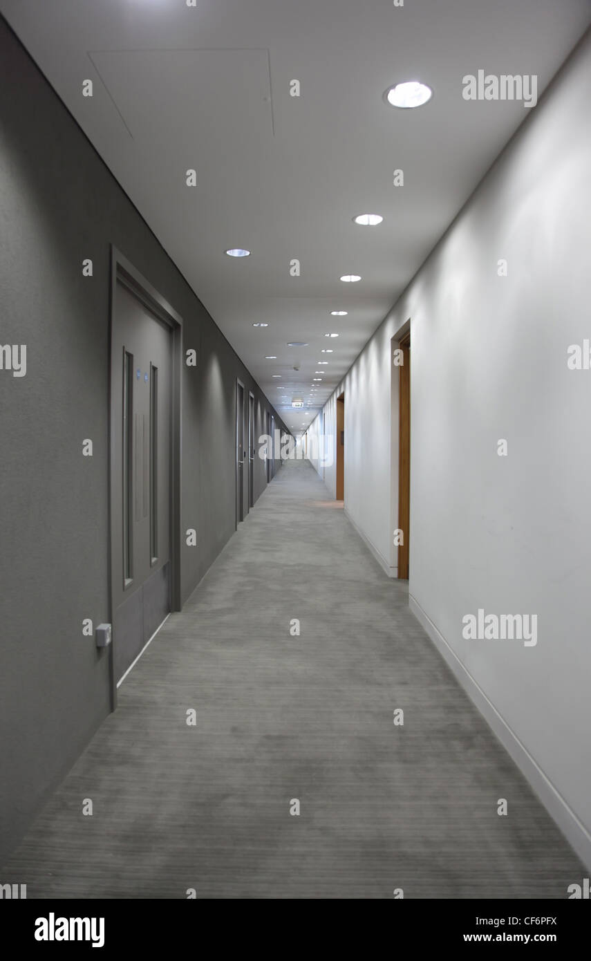 einen langen grauen Flur mit Türen. Licht am Ende des Korridors Stockfoto