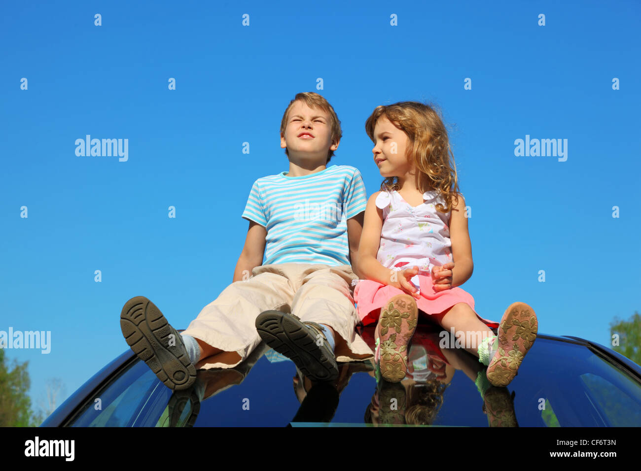 kleine Jungen und Mädchen sitzen auf Autodach auf blauen Himmel Stockfoto