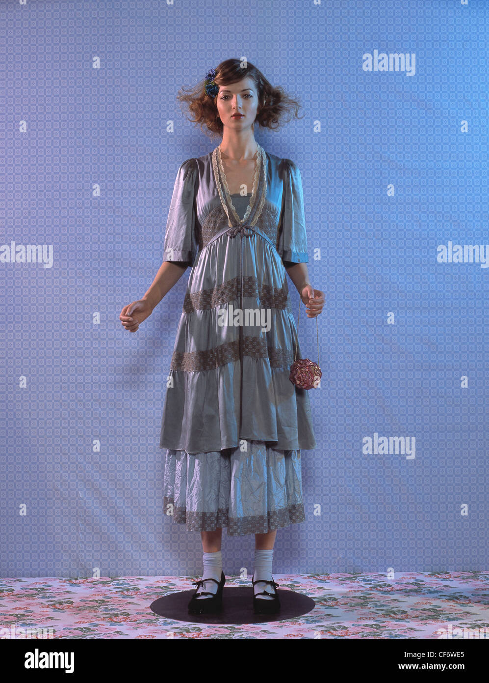 Weibliche Brünette welliges Haar abgeschnitten auf einer Seite blaue Blume tragen zerknitterten blauen satin-Kleid floral Saum unter kürzere blau satin Stockfoto