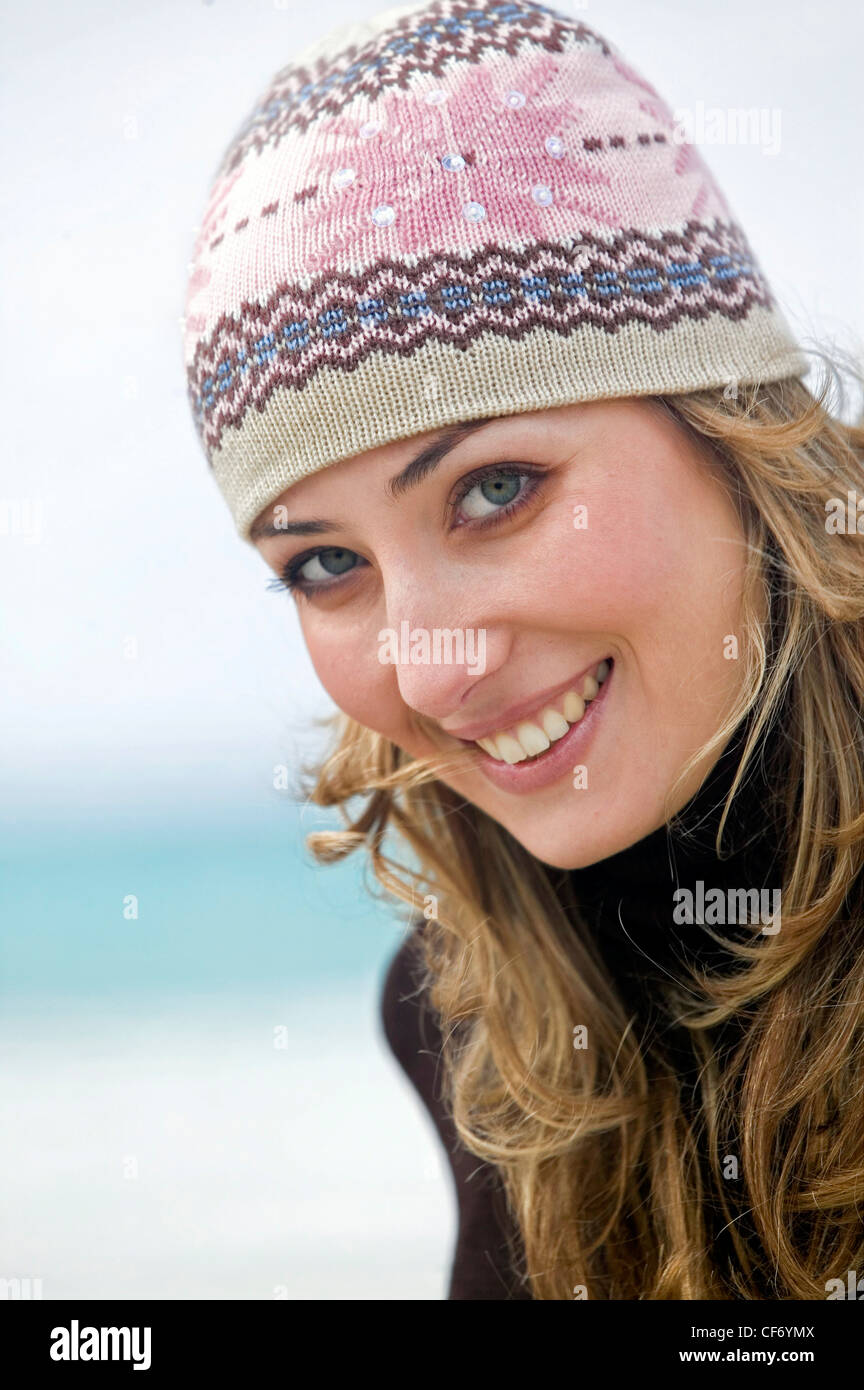 Weibliche blonde lange Haare tragen, rosa, Creme und braun Strickmütze und braun Rollkragen Blick seitwärts um die Kamera zu Lächeln Stockfoto