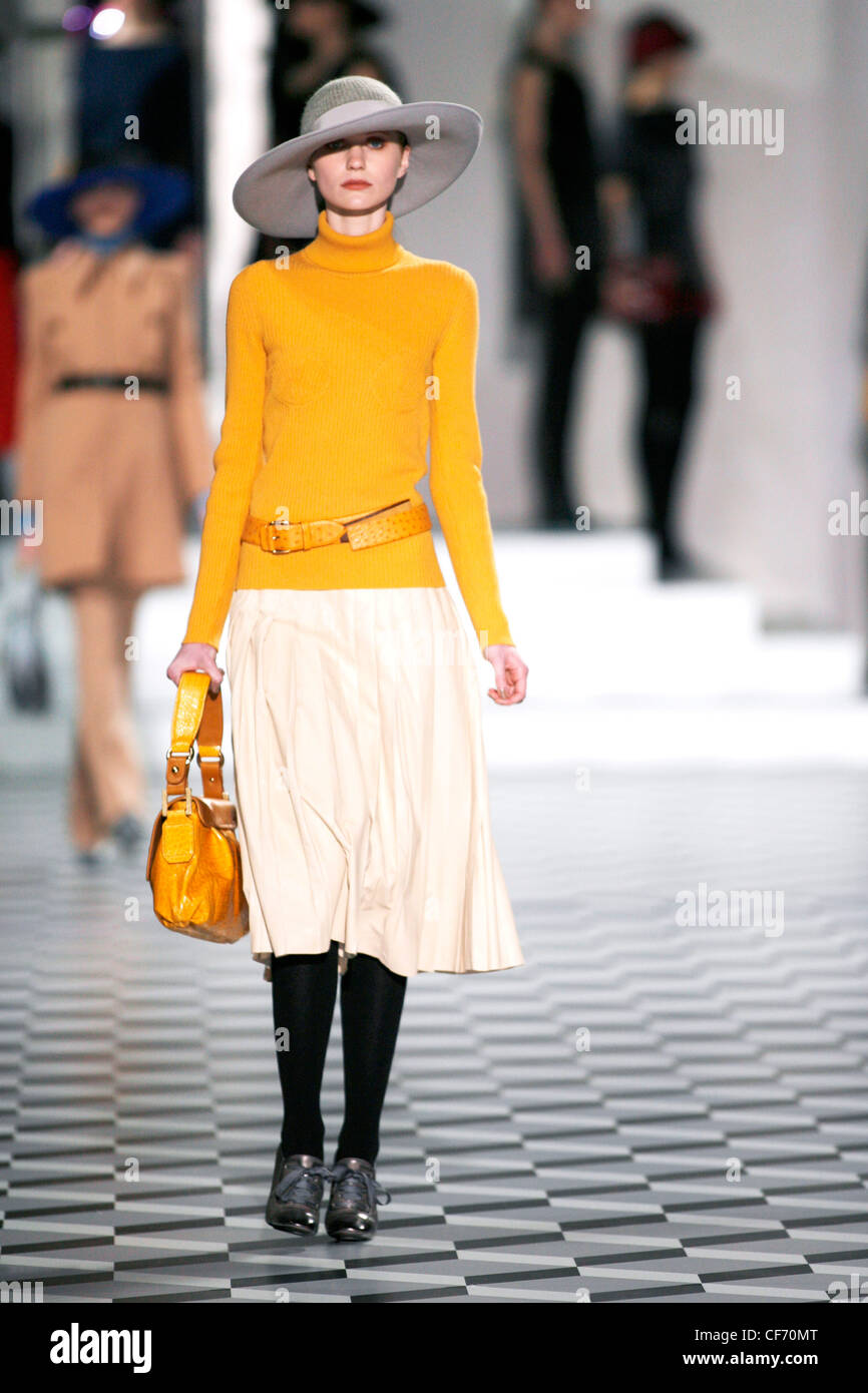 Modell Jeanette trägt graue Wolle und Filzhut gelben Rollkragen und Creme Falten eine Linie Rock, schwarze Strumpfhose und grau Stockfoto