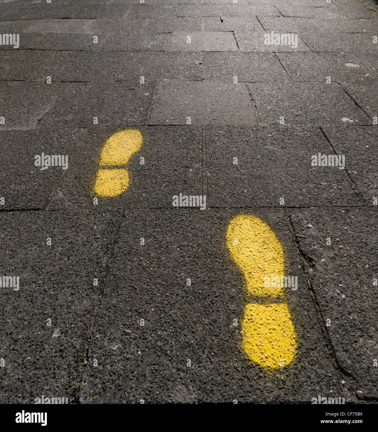 gelben Fußabdrücke auf einem Bürgersteig Stockfoto