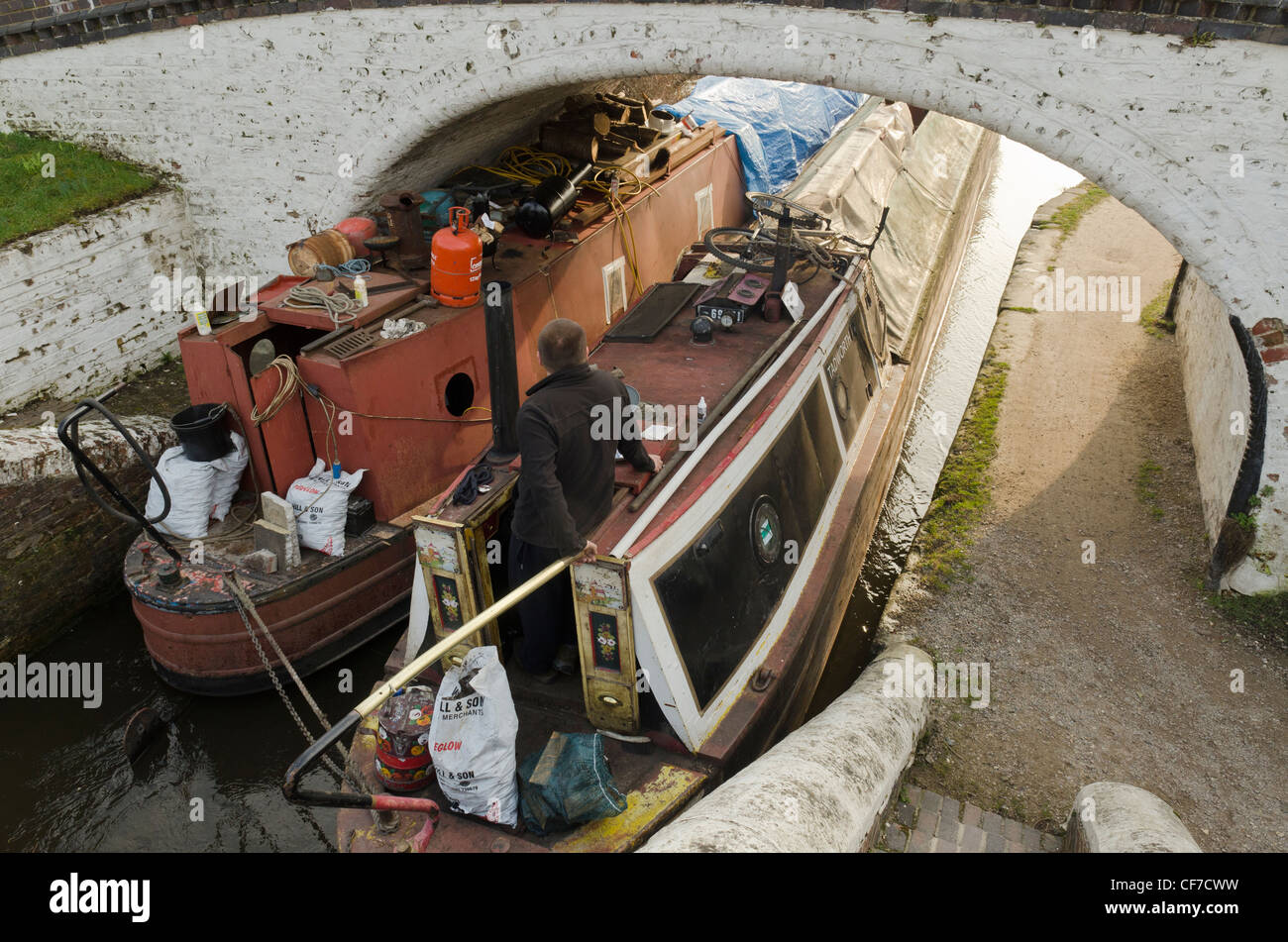 Ein Mann führen zwei schmale Boote unter eine Kanalbrücke bei Stocker Lock Grand Union canal Rickmansworth Herts UK Stockfoto