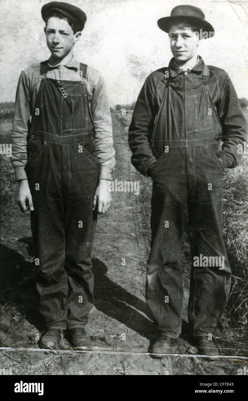 Zwei Bauernjungen in Overalls stehen für ein Porträt in einem Feld während der 1920er oder 1930er Jahren Weltwirtschaftskrise Landwirtschaft Herren Mode Brühe Stockfoto