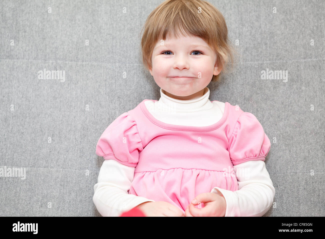 Porträt des kleinen kaukasischen russische Mädchen im rosa Kleid auf Couch sitzen und Lächeln Stockfoto