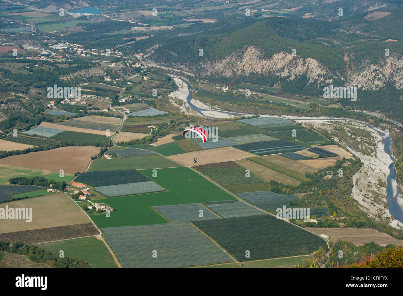 Ein Gleitschirmflieger schweben hoch über dem Talboden mit landwirtschaftlich genutzten Flächen unter in Le Chabre, Provence. Stockfoto