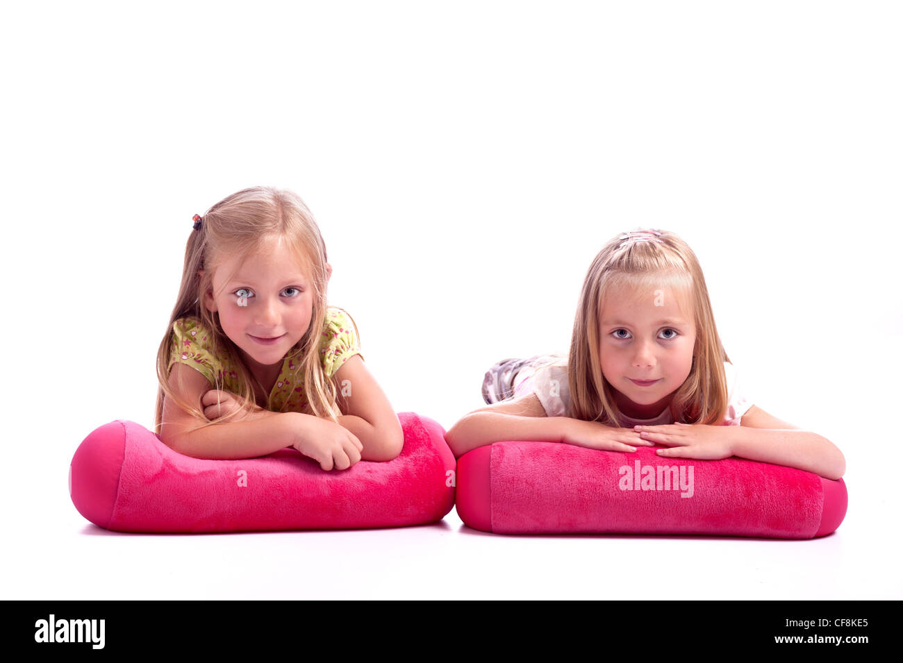 zwei kleine Mädchen liegend ein rosa Kissen Spaß. isoliert auf weißem Hintergrund Stockfoto