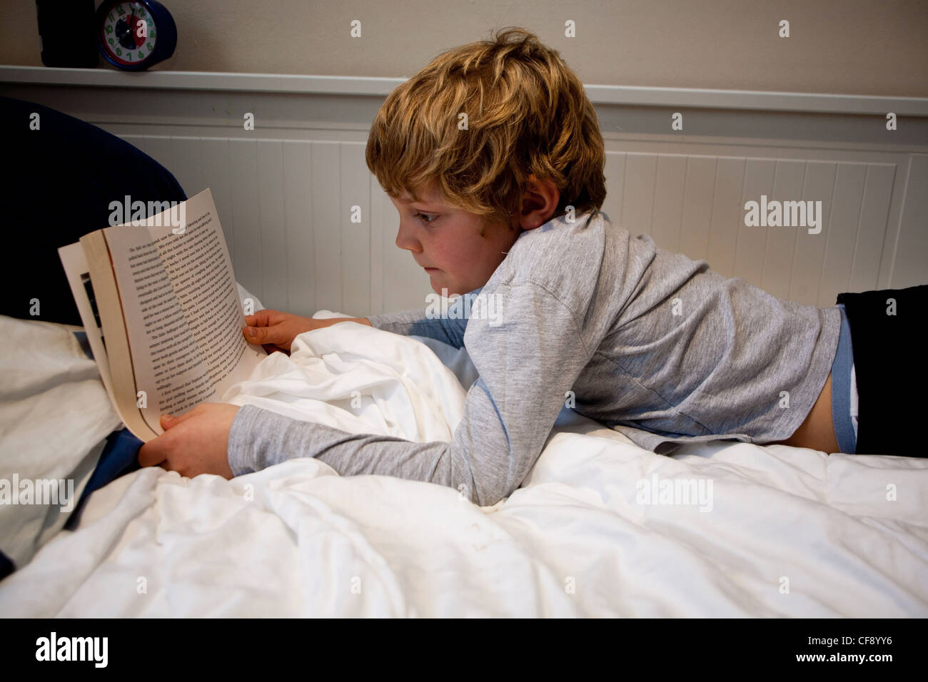Ein Junge mit einem Buch in seinem Schlafzimmer Stockfoto