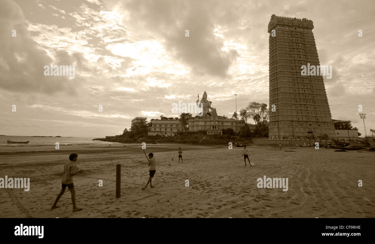 Kinder spielen Cricket am Strand mit Shiva-Tempel im Hintergrund Stockfoto