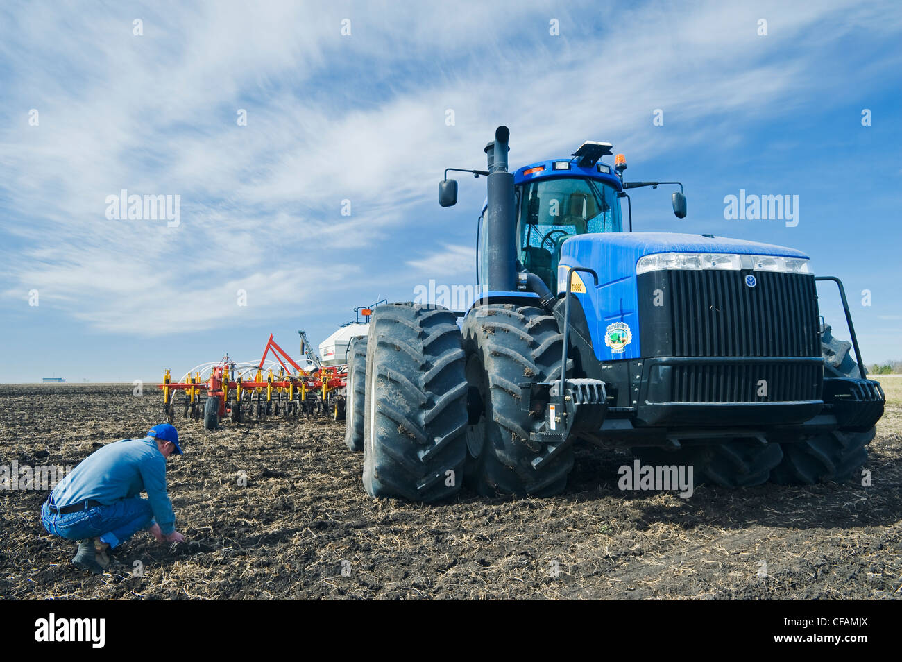 ein Mann untersucht Boden, Traktor und Luft bis Sämaschinen im Hintergrund, in der Nähe von St. Agathe, Manitoba, Kanada Stockfoto