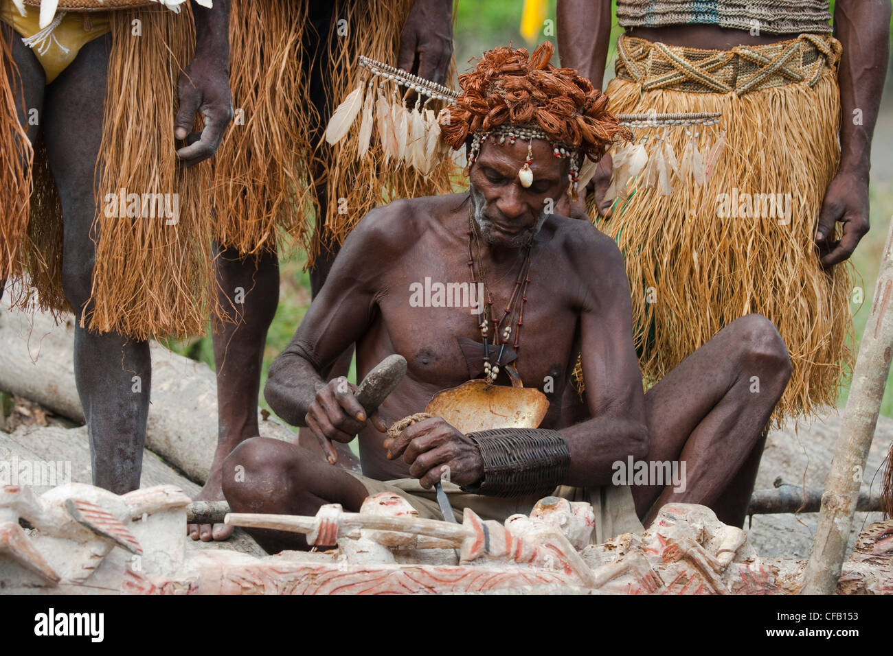 Mann vom Stamm Asmat schnitzen mit einem Meißel, Agats Dorf, Neu-Guinea, Indonesien Stockfoto