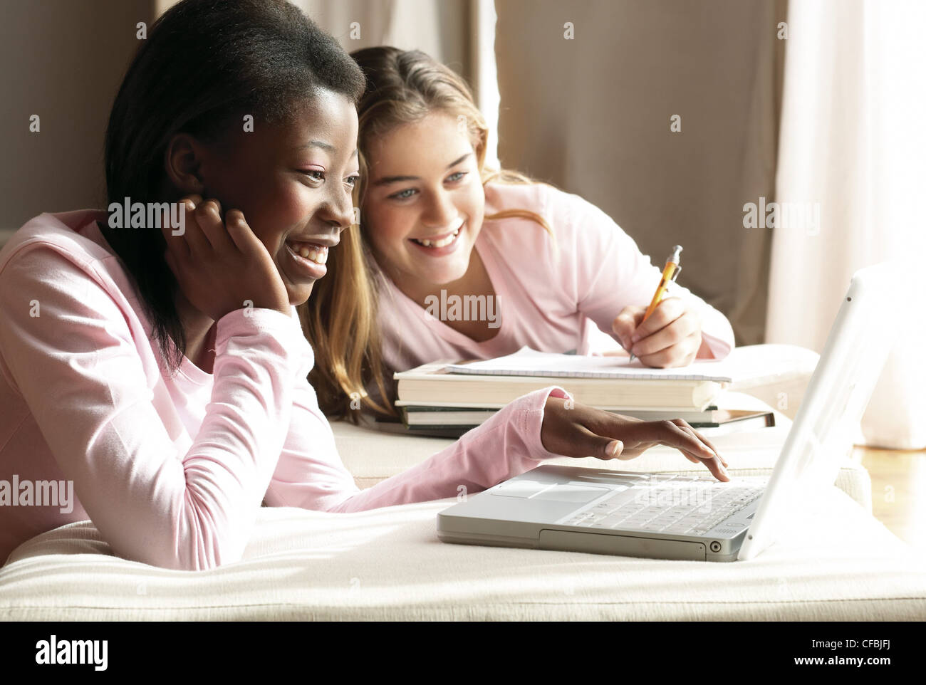 Zwei Mädchen beide trägt eine rosa lange Ärmel Top Mädchen langes blondes Haar schreiben auf Notizpapier stützte sich auf Bücher, Mädchen schwarze Haare Stockfoto