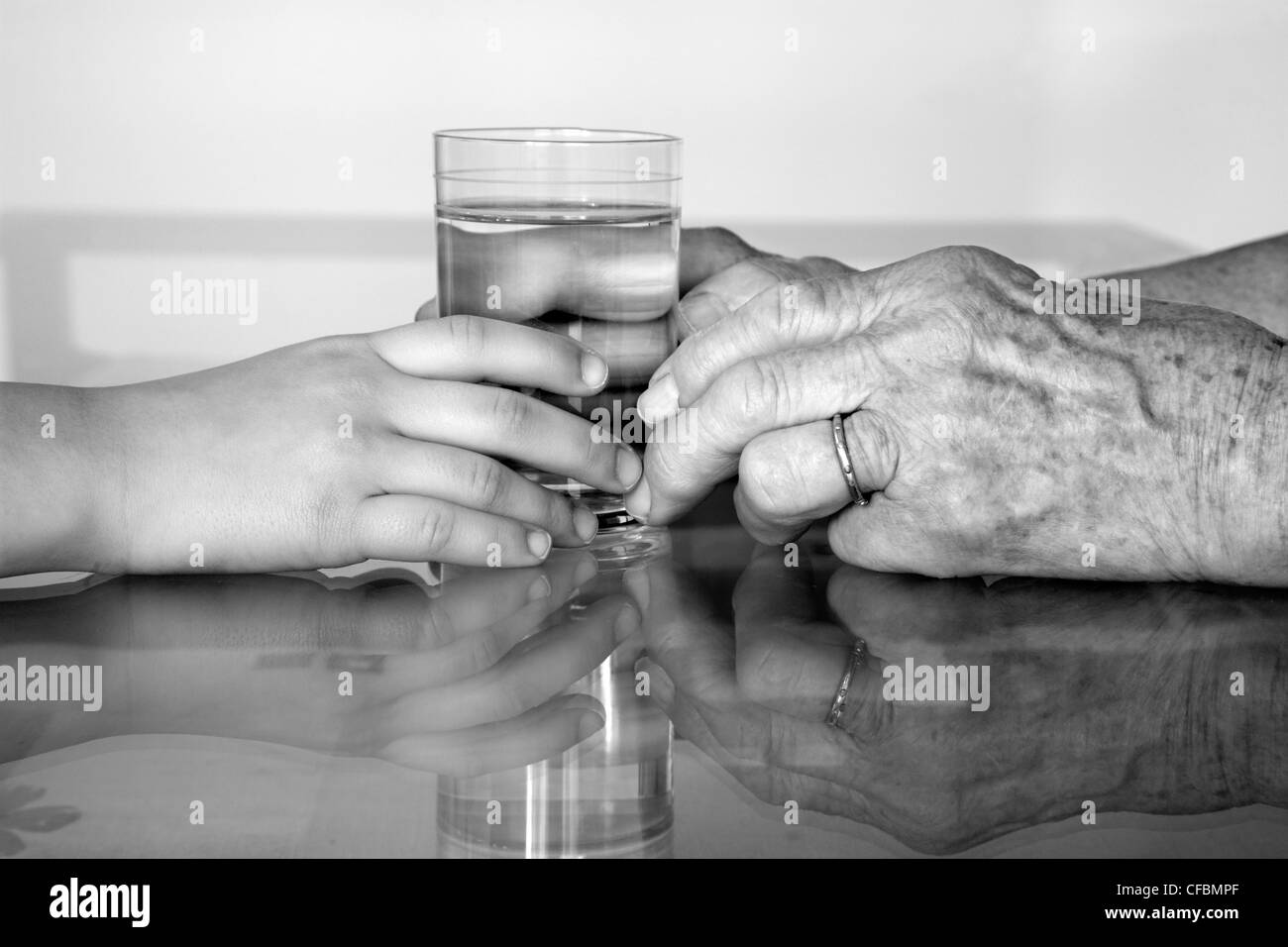 Händen der Großmutter und Enkel mit dem Glas Wasser Stockfoto