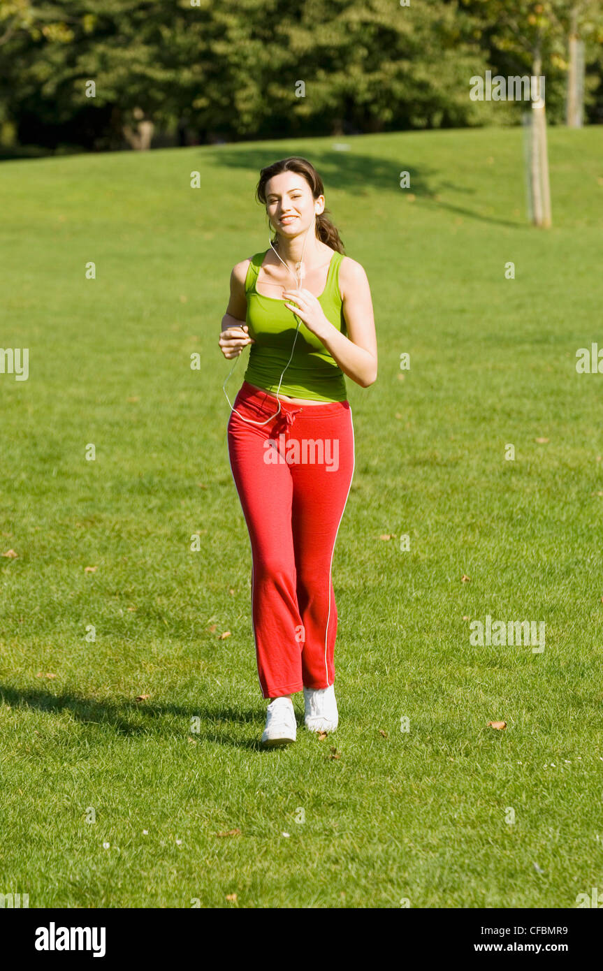 Weibliche rote Hosen, grüne Weste Top und weiße Trainer im Park hören mp Player laufen Stockfoto