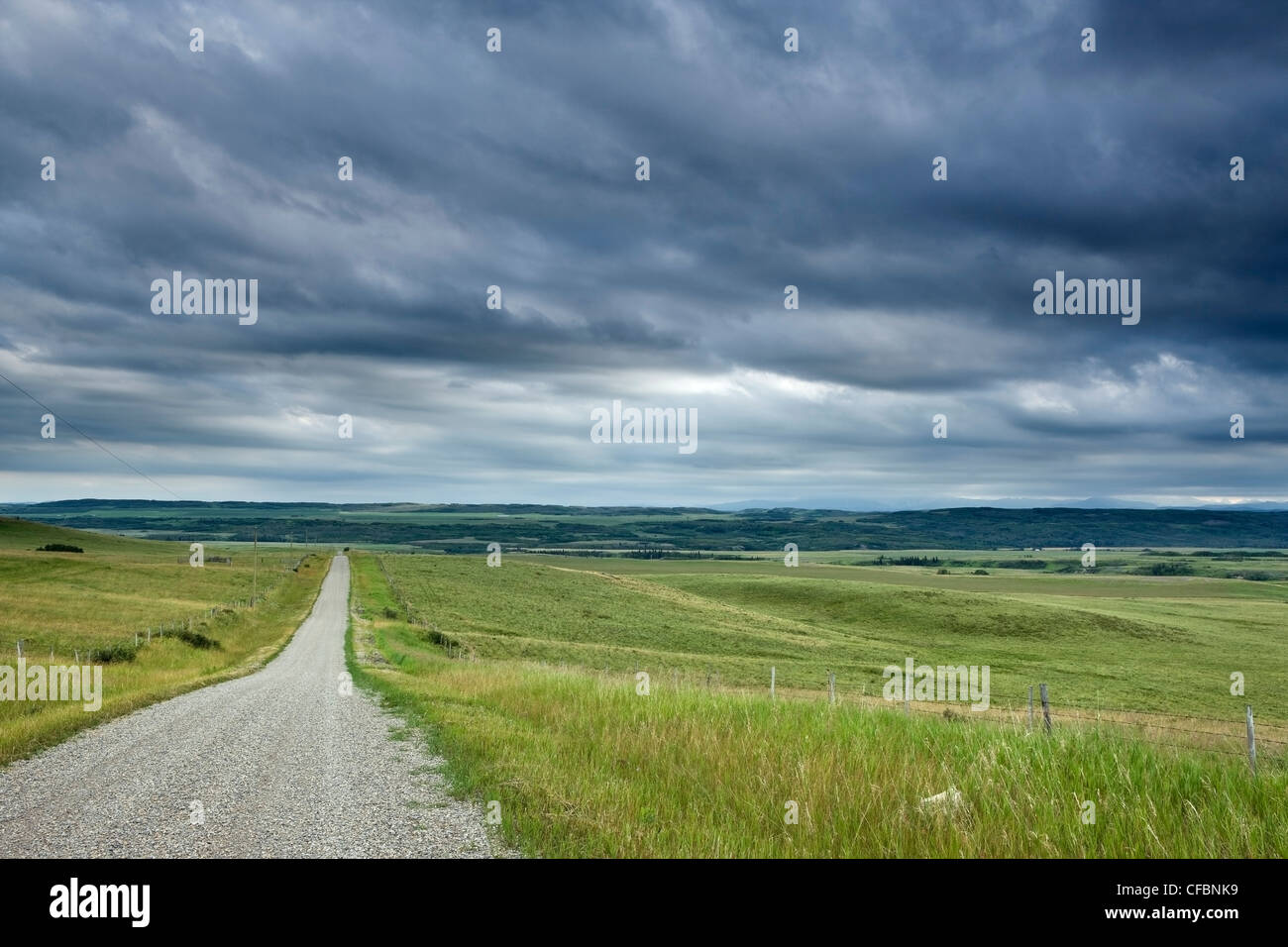 Landstraße, Feld und Zaun mit Gewitterwolken in der Nähe von Cochrane, Alberta, Kanada Stockfoto
