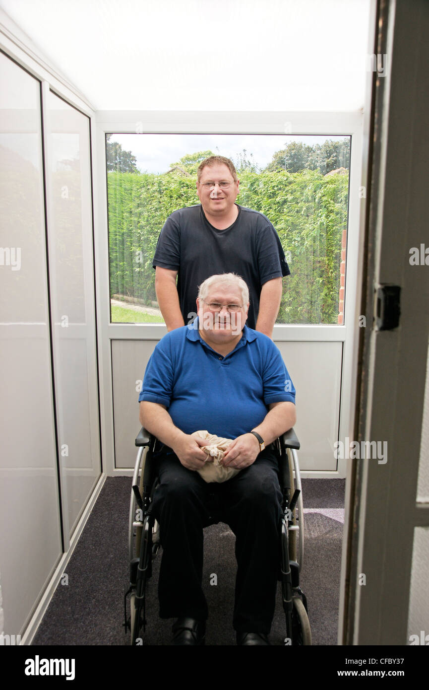 älteren Mann im Rollstuhl deaktiviert mit seinem Betreuer Sohn gedrängt im Innenbereich von Veranda, Halle Stockfoto