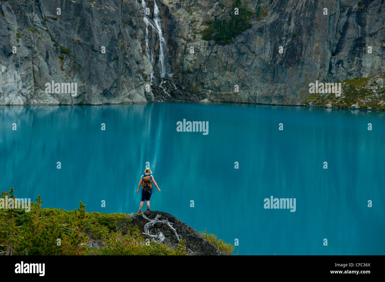 Eine junge Frau Wanderungen vor einem blauen See und Wasserfall in der Niut Range, British Columbia, Kanada Stockfoto