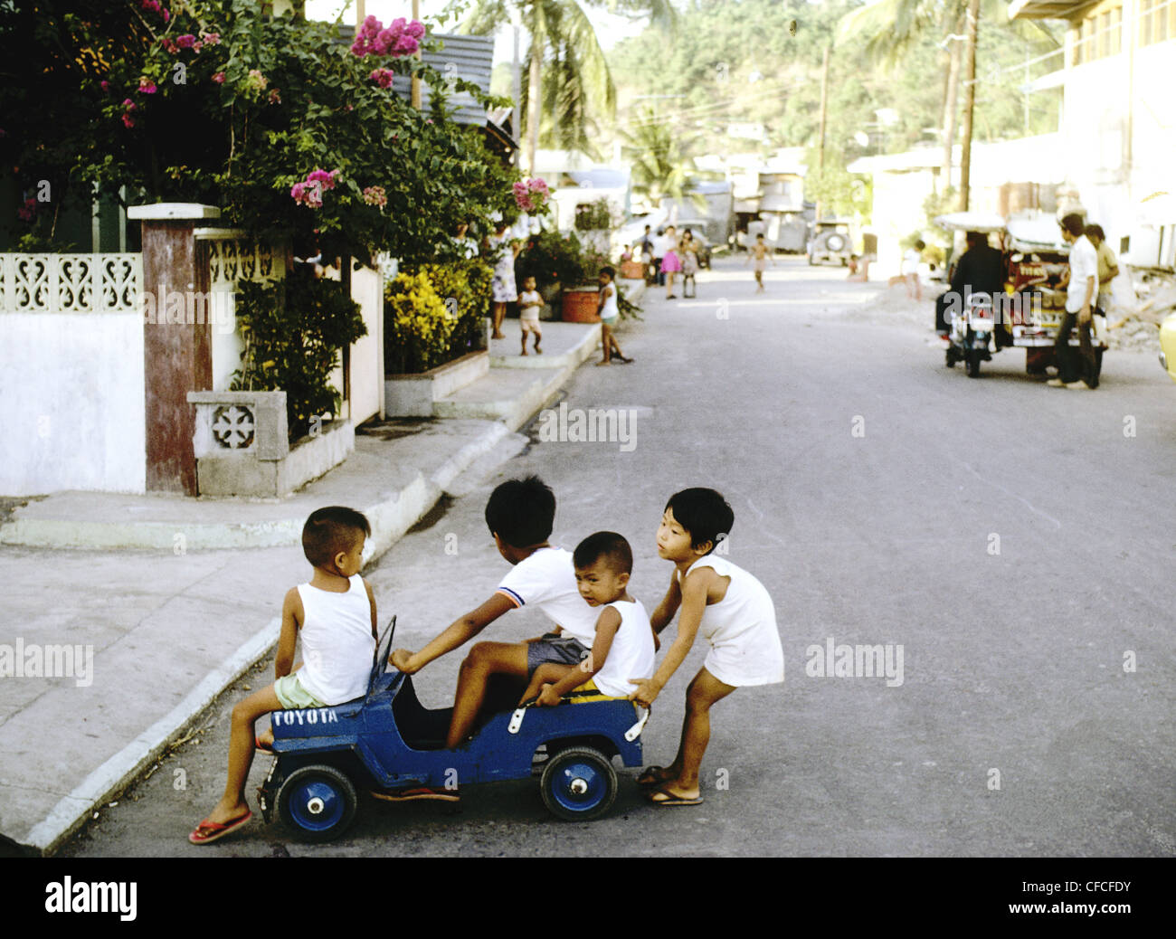 Vier junge Kinder teilen sich einen Spielzeug des 2. Weltkrieges Jeep auf einer grünen Seitenstraße einer Provincaial Stadt in den Philippinen- Stockfoto