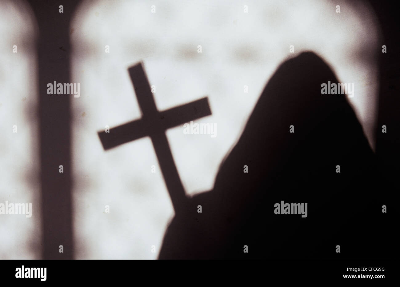 Vermummten Mönch hält große Kruzifix und Silhouette gegen helle weiße Wand mit Fenster Schatten Stockfoto