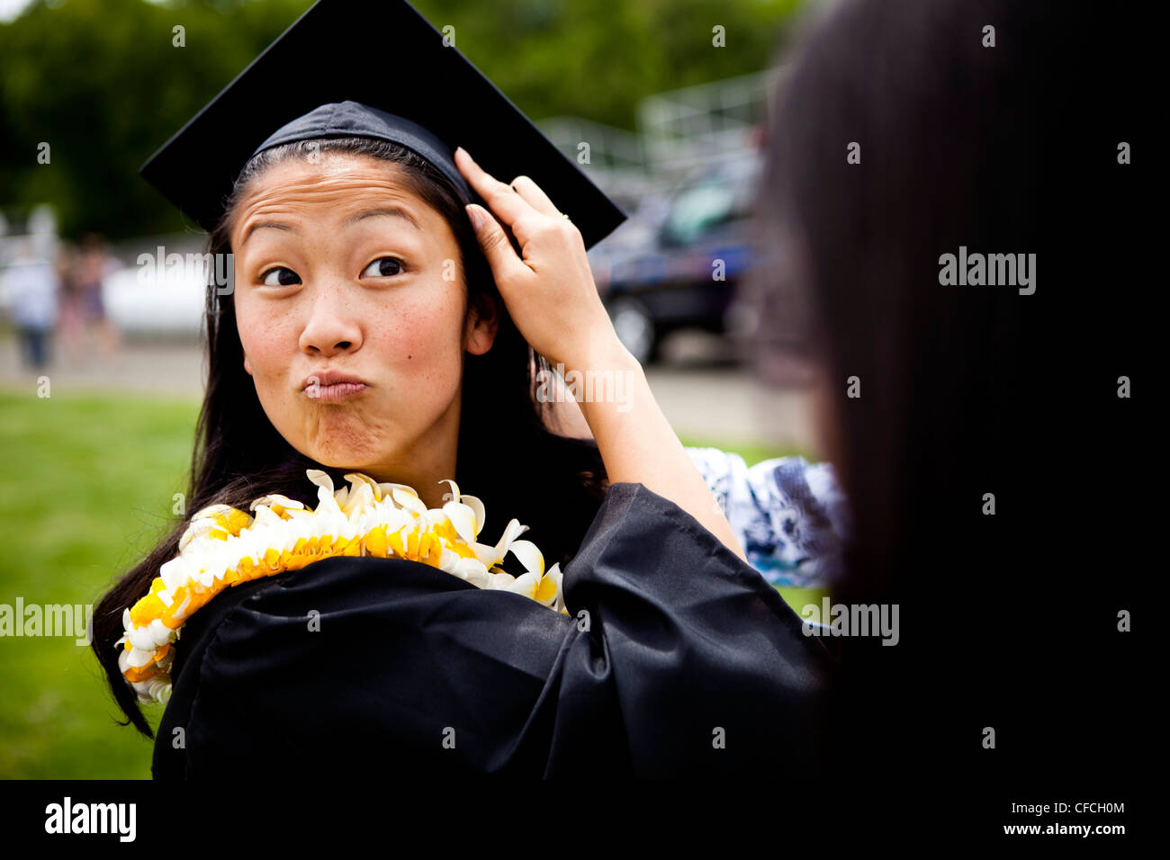 Eine Absolventin macht lustige Gesichter, während sie an ihrem Abschlussfeiertag von der Universität New Have in hawaiianische Lei (Lays) gehüllt ist Stockfoto