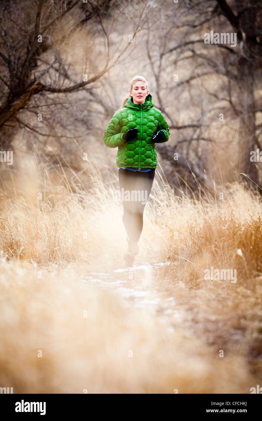 eine junge Frau läuft nach unten Weg Tote Gras nördlich von Dixon Reservoir an einem kalten Tag in einer grünen Daunenjacke. Stockfoto