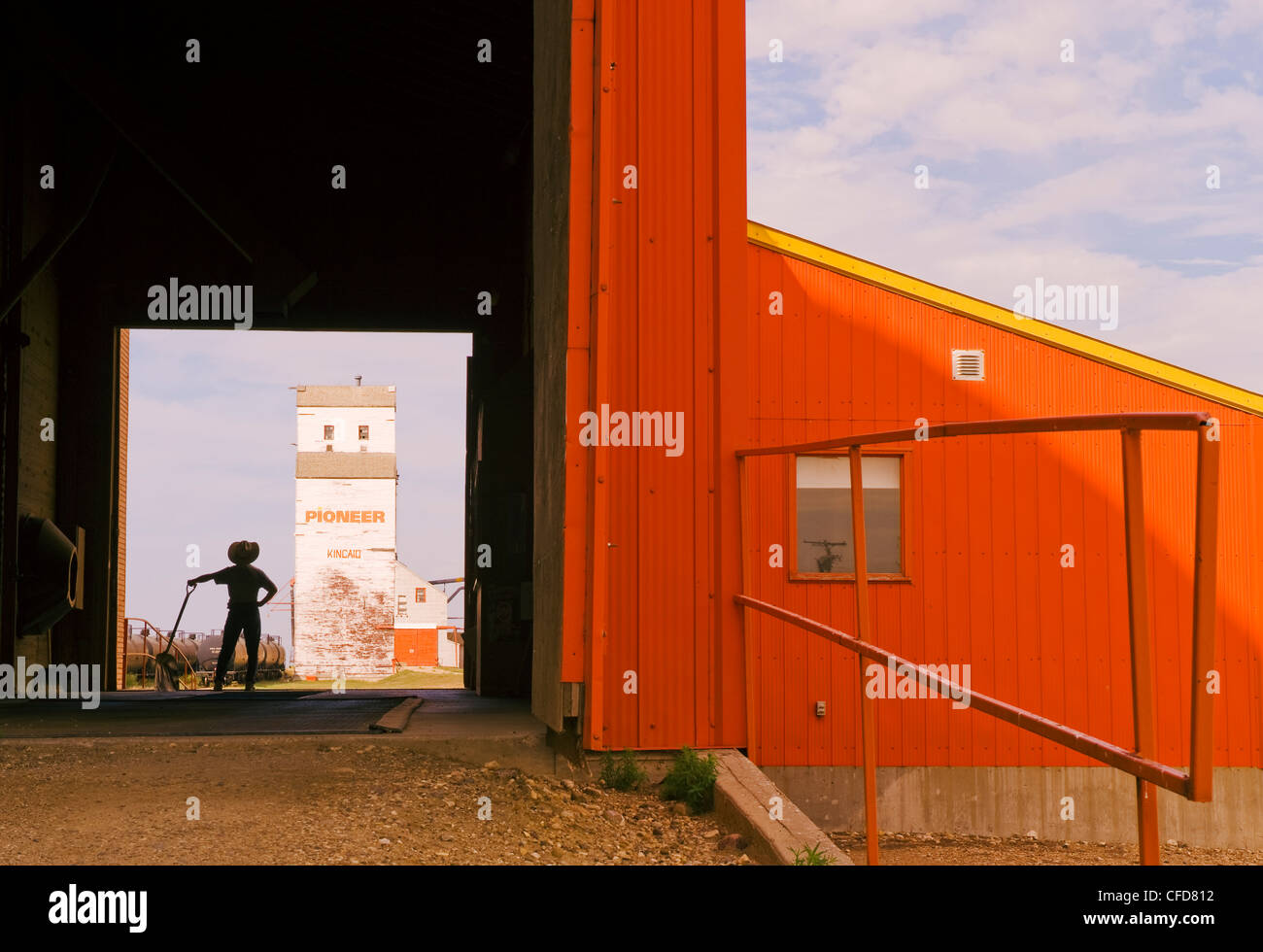 Ein Mann hält eine Schaufel blickt auf eine alte Kornlift, Kincaid, Saskatchewan, Kanada Stockfoto