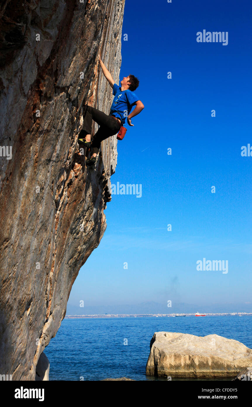 Ein Bergsteiger befasst sich eine schwierige Route auf den Klippen von Akyalar, mit der Stadt Antalya in der Ferne, Anatolien, Türkei Stockfoto