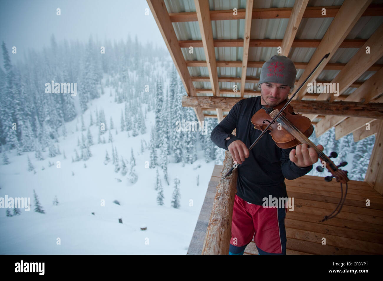 Ein Mann nimmt eine Auszeit vom Skitouren um etwas Musik zu machen. Eisfall Lodge, Golden, British Columbia, Kanada Stockfoto