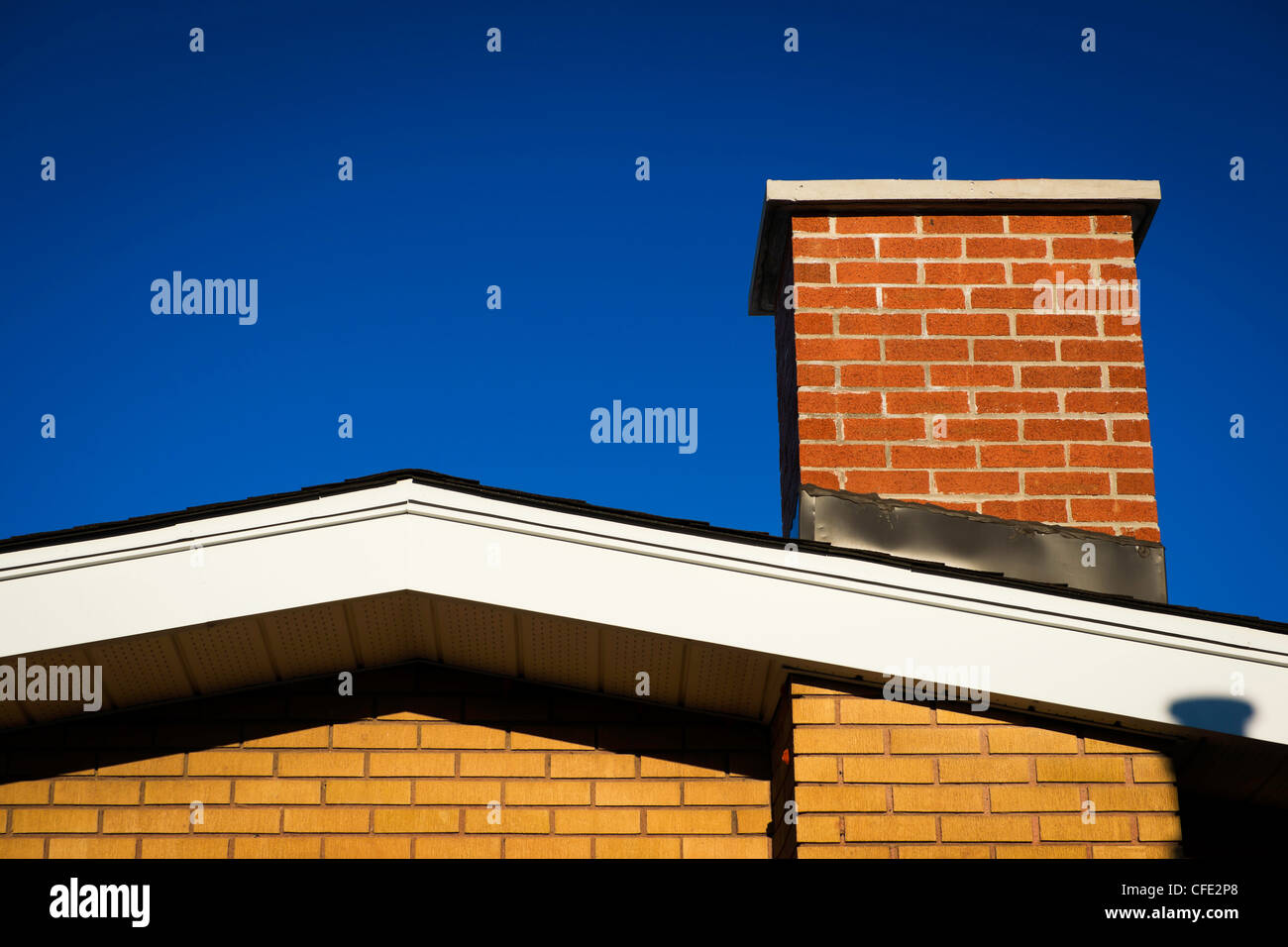 Am Giebel des ein Ziegelhaus mit gemauerten Schornstein in hellem Sonnenlicht, vor einem tiefblauen Himmel. Stockfoto
