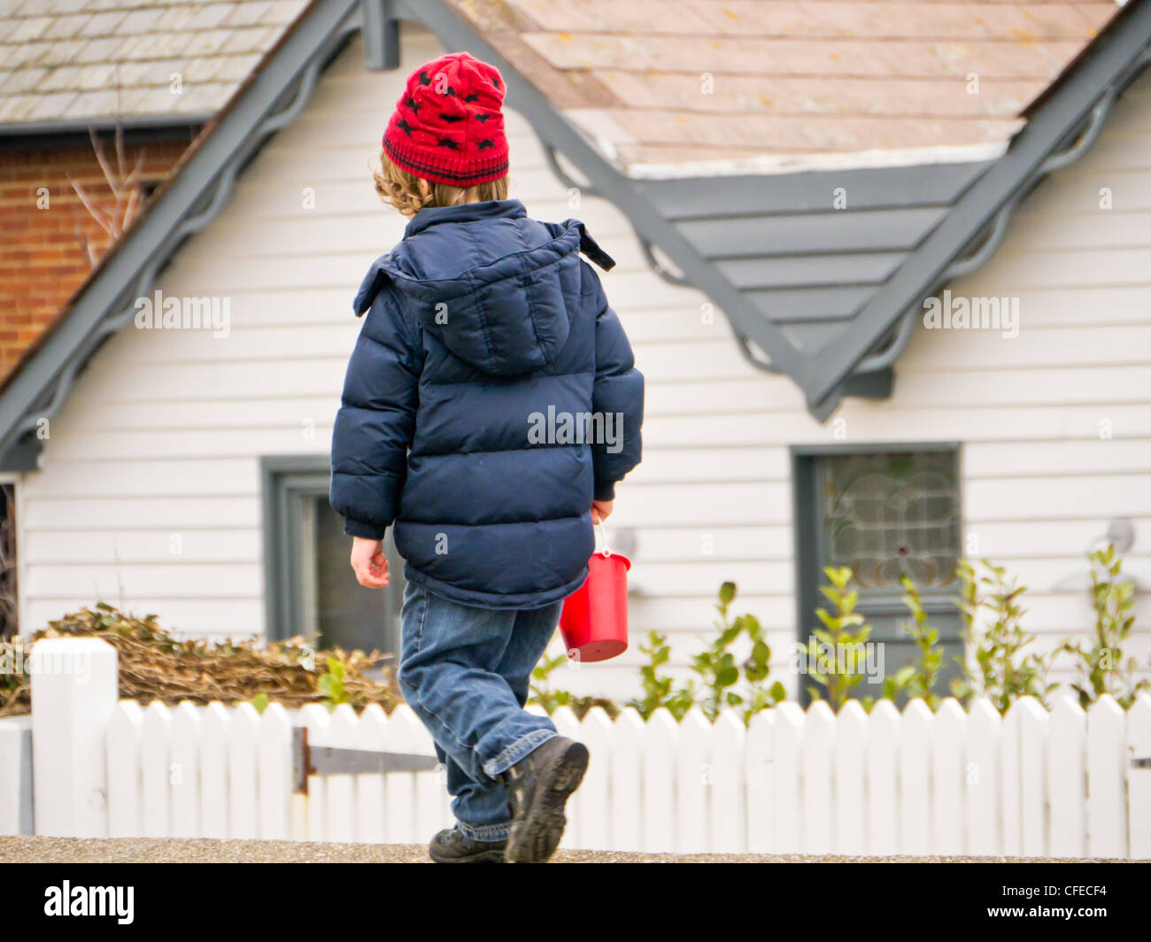 Kleines Kind zu Fuß entlang einer Wand mit einem Eimer und roten Hut in Whitstable, Kent, Großbritannien. Stockfoto