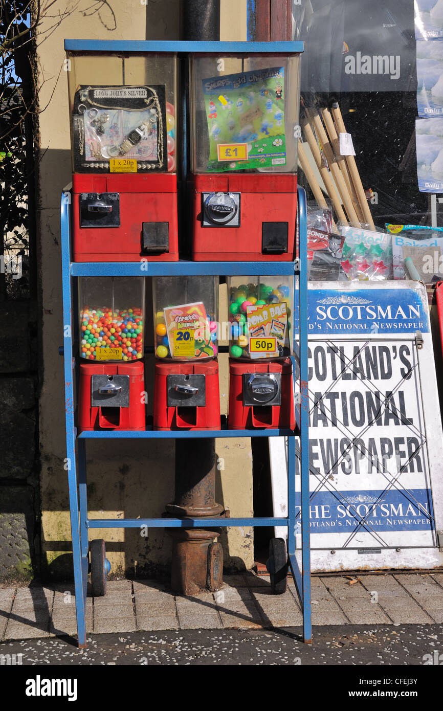 Retro-Münz Stil süße Dispenser und Zeitungsanzeige außerhalb ein Zeitschriftenladen in Nina, Scotland, UK Stockfoto