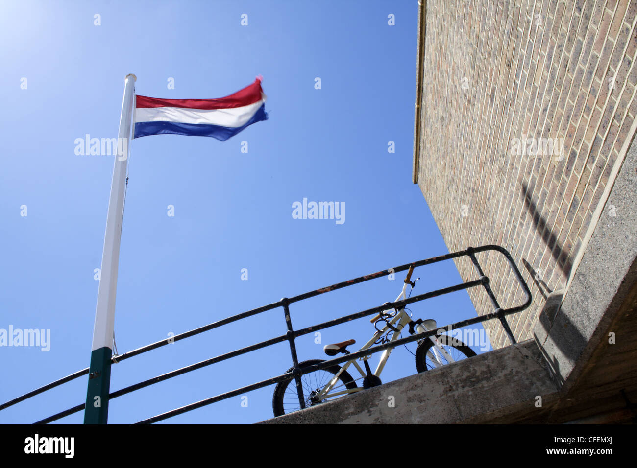 Eine Flagge auf die Niederlande, fast identisch mit der der Luxemburger Flagge fliegt vor einem blauen Himmel. Ein Mountainbike ist geparkt. Stockfoto