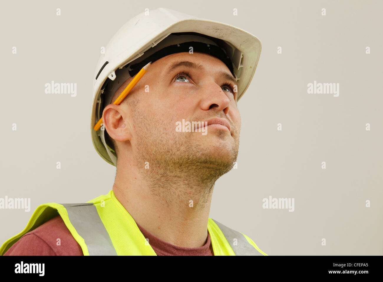 Modell stellte einen Arbeiter tragen Schutzhelm, hi-Vis-Jacke und Bleistift hinter dem Ohr Stockfoto