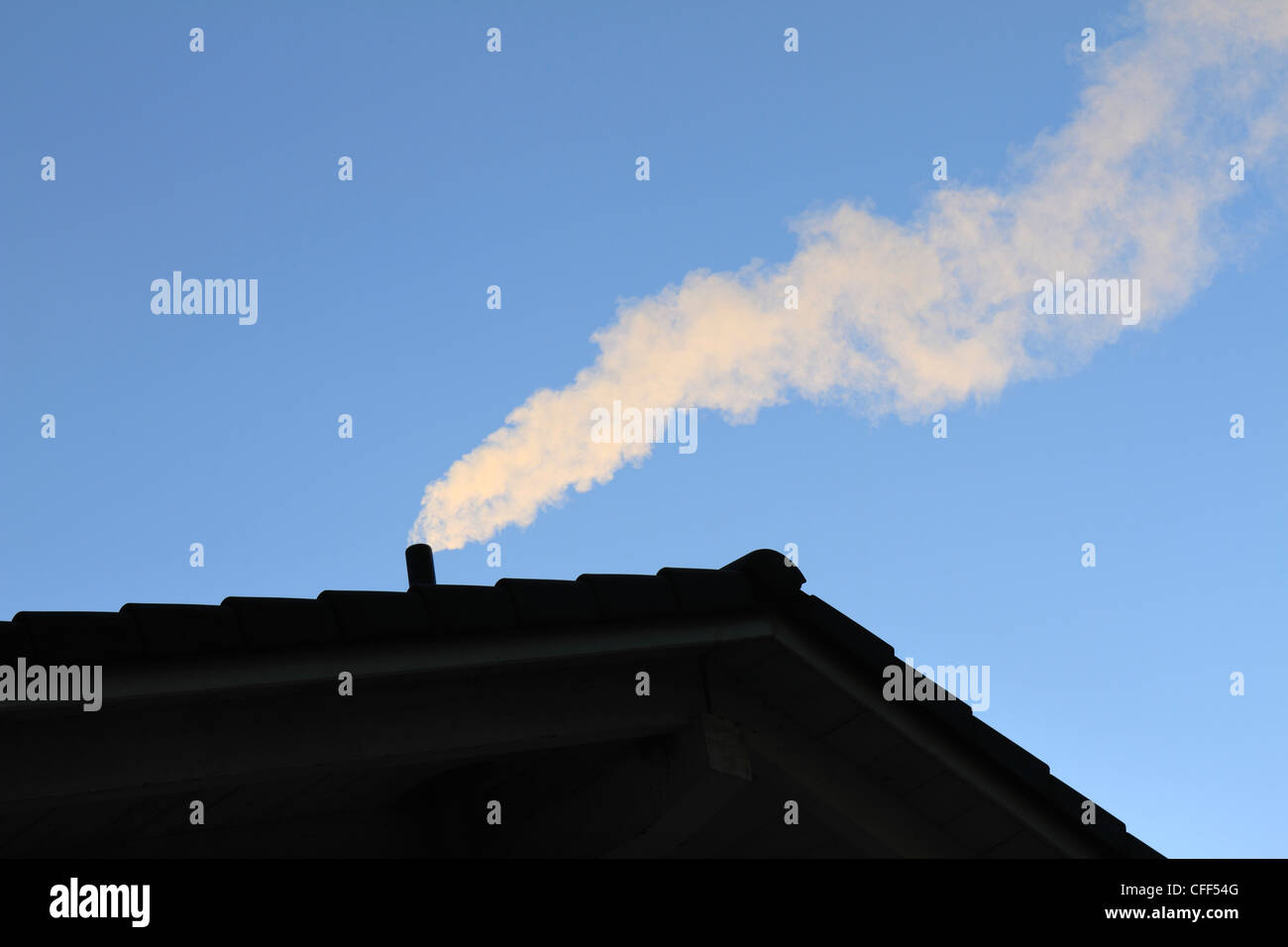 Rauch aus einem Schornstein mit blauem Himmel als Hintergrund, obere Bayern Chiemgau Stockfoto