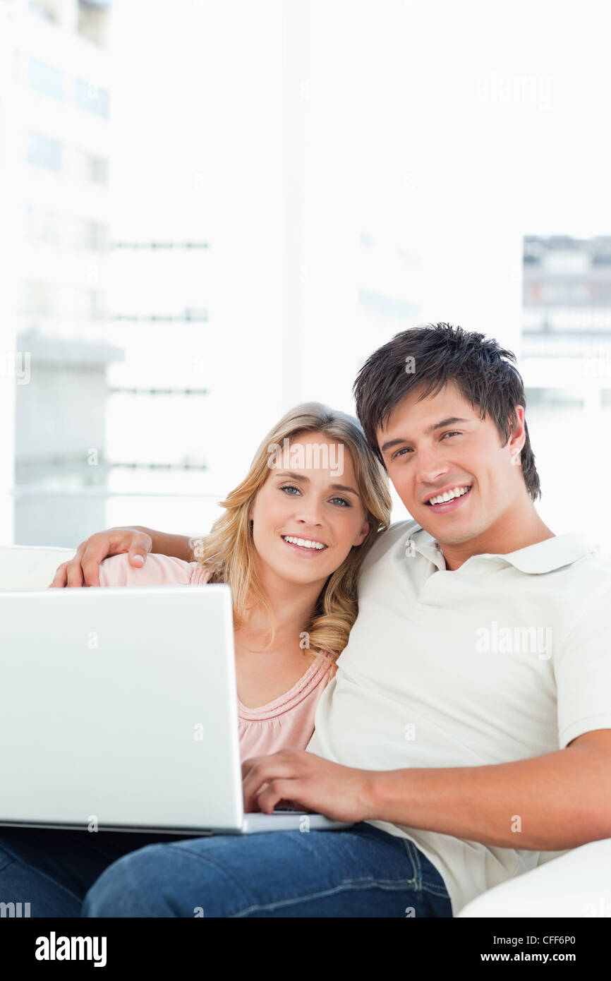 Mann und Frau suchen, geradeaus, wie sie den Laptop auf der Couch verwenden Stockfoto
