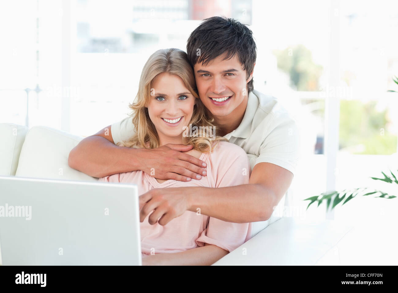 Mann die Frau umarmen, da sie das Notebook nutzen und geradeaus schauen Stockfoto