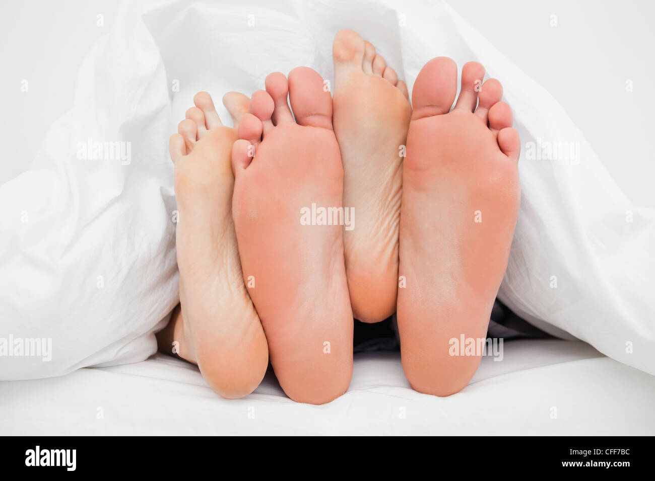 Zwei Paar Füße gekreuzt übereinander im Bett Stockfoto